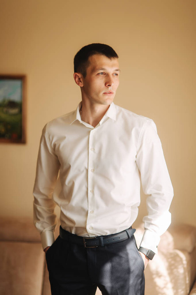 Handsome man in shirt on his wedding day. He stand hear the window - Foto, afbeelding