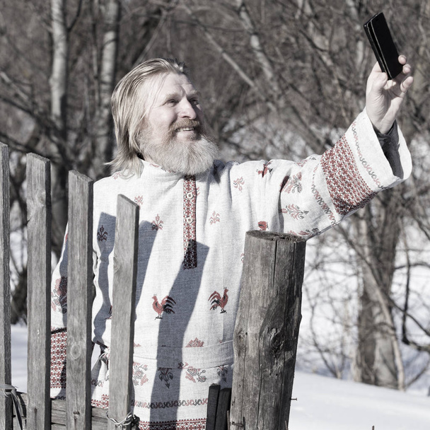 Slavic man in a beautiful national painted shirt on a spring day on the earth makes selfy - Photo, Image