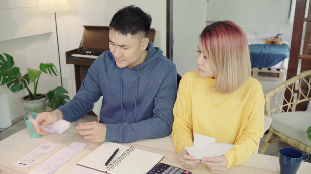 junge gestresste asiatische Paare verwalten ihre Finanzen und überprüfen ihre Bankkonten mit Laptop und Taschenrechner zu Hause. Frau und Mann erledigen gemeinsam Papierkram und zahlen online Steuern. - Filmmaterial, Video