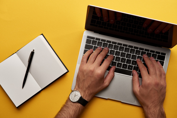 cropped shot of man working with laptop and notebook on yellow surface - Фото, изображение