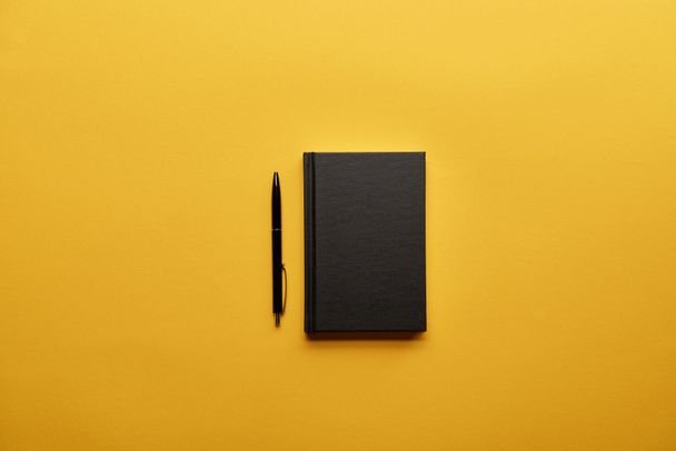 top view of closed notebook and pen on yellow surface - Φωτογραφία, εικόνα