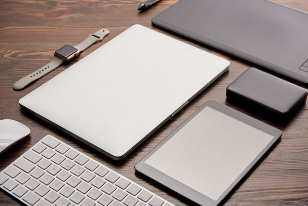 close-up shot of various wireless gadgets and graphics tablet on wooden desk - Photo, Image