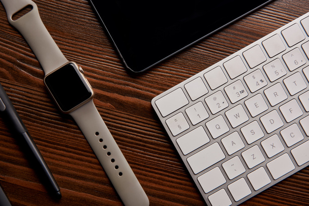 вид сверху на умные часы с беспроводной клавиатурой и графическим планшетом на деревянном столе
 - Фото, изображение