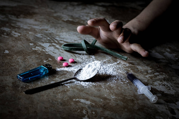 Día Internacional contra el Abuso de Drogas. Mano humana joven tratando de llegar a la cuchara de heroína cocida en el suelo de hormigón grueso. Concepto de adicción a las drogas y síntomas de abstinencia. Copiar espacio
.  - Foto, Imagen