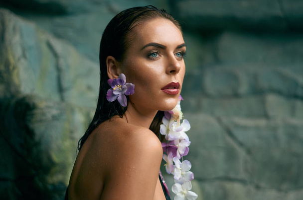 岩に熱帯の花の形のピアスと魅力的な若い女性の肖像画 - 写真・画像