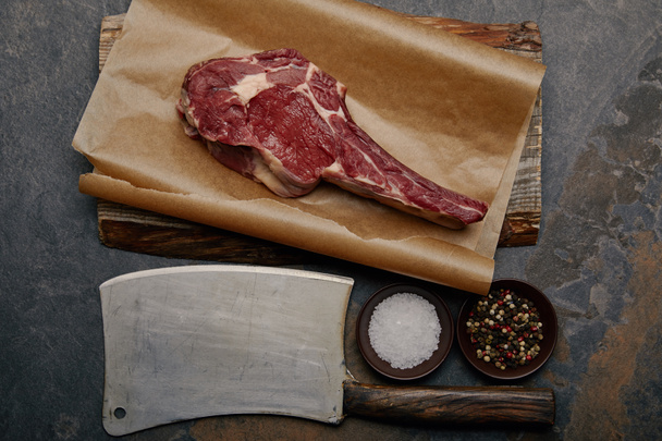 top view of raw rib eye steak on baking paper with butcher knife, spices  - Фото, зображення