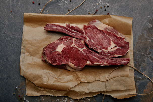 top view of raw rib eye steaks on baking paper with spices on grey background - Фото, зображення