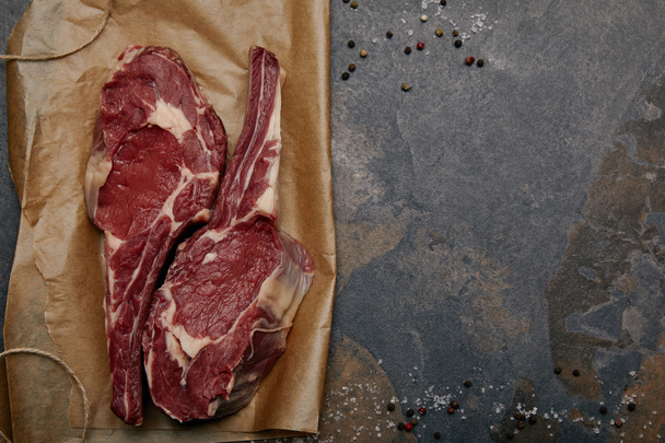 pohled shora na syrové steaky na pečícím papírem s kořením na šedém pozadí - Fotografie, Obrázek