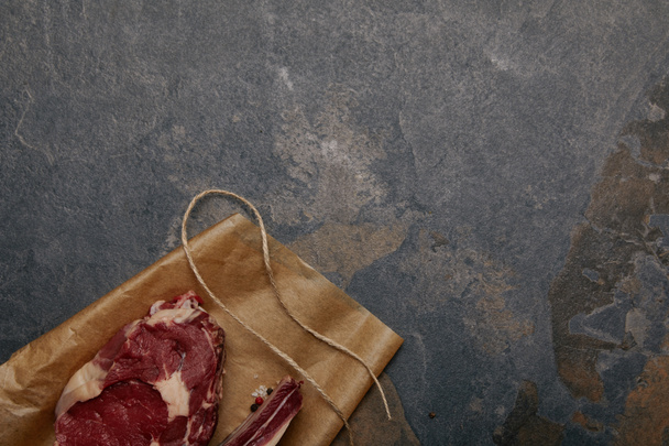 κάτοψη του ωμό κρέας φιλέτο στην λαδόκολλα σε γκρίζο φόντο - Φωτογραφία, εικόνα