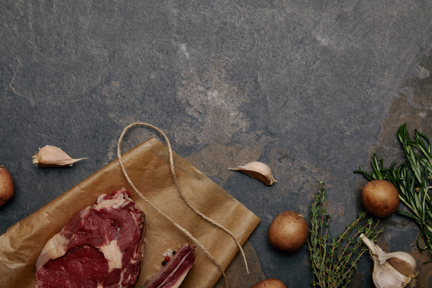 灰色の背景にジャガイモと紙を焼く生肉ステーキのトップ ビュー - 写真・画像