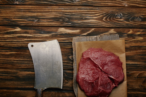 top view of raw meat on baking paper with butcher knife on wooden background - Photo, Image