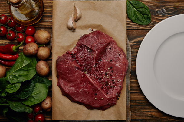 flat lay with fresh raw meat on baking paper with vegetables and spinach on wooden background - Photo, Image