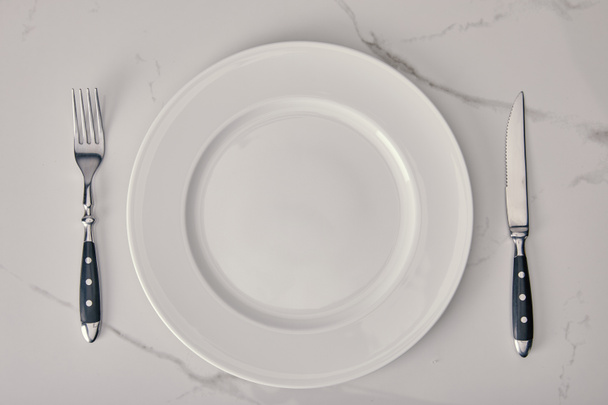 plato vacío con tenedor y cuchillo sobre fondo de mármol blanco
 - Foto, Imagen