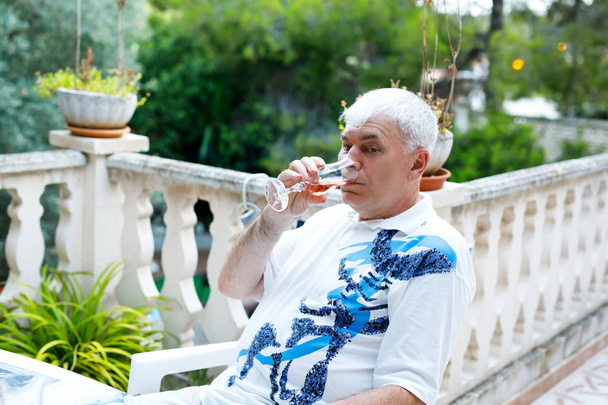 Hombre mayor de 60 años bebiendo un vaso de vino de rosas de vacaciones. Hombre jubilado disfrutando de la cálida noche de verano
 - Foto, imagen