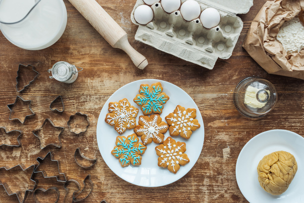flat lay with Christmas cookies on plate, ingredients and cookie cutters arranged on wooden tabletop - Fotografie, Obrázek
