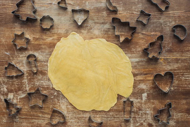 leigos planos com massa crua e cortadores de biscoitos de Natal na superfície de madeira
 - Foto, Imagem