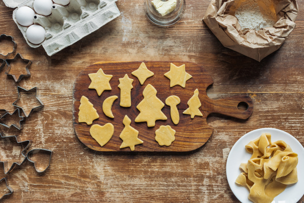 flat lay with cut raw dough for christmas cookies baking on cutting board on wooden surface - Foto, imagen