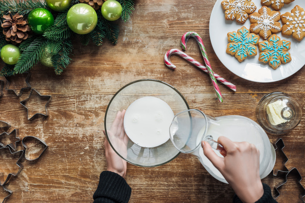 tiro recortado de la mujer que vierte la leche en el tazón mientras que hace la masa para las galletas de Navidad en la superficie de madera
 - Foto, Imagen