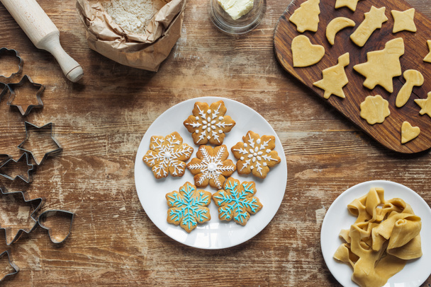 flat lay with Christmas cookies on plate, ingredients and cookie cutters arranged on wooden tabletop - Foto, immagini