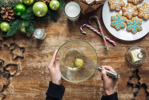 cropped shot of woman with whisk making dough for christmas cookies on wooden tabletop with decorative wreath - Fotó, kép
