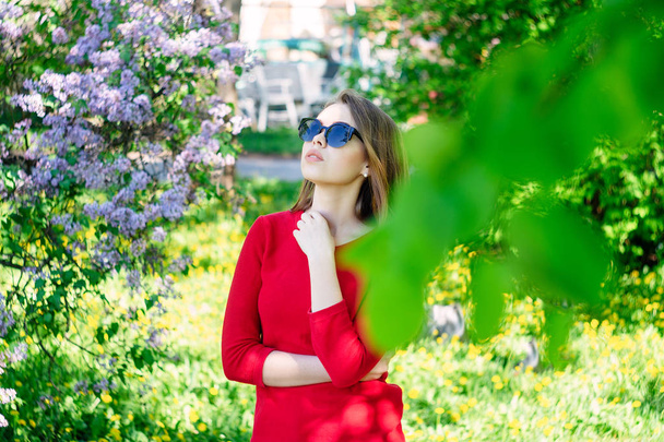 Young beautiful girl in the spring in the park stands in the circle of lilac blossom. In sunglasses. - Φωτογραφία, εικόνα