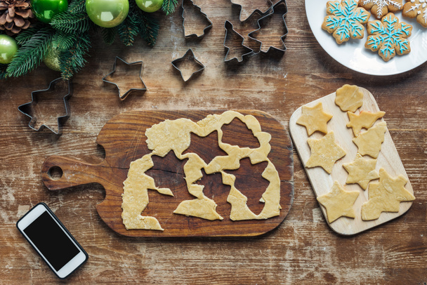 top view of smartphone with blank screen, raw dough for christmas cookies and cookie cutters on wooden surface - Photo, Image