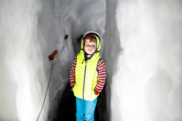 Egy kisfiú, biztonsági sisakkal a gleccser belsejében, jégalagúttal. Iskolásgyerek túrázás és felfedezés hegy Tirol, Ausztria, Hintertux. - Fotó, kép