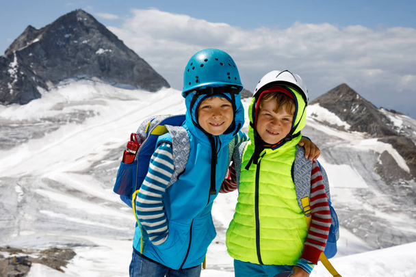 Two little boys with safety helmets and clothing with mountains landscape backgrounds. Kids hiking and discovering glacier in Tirol, Austria, Hintertux - Photo, Image