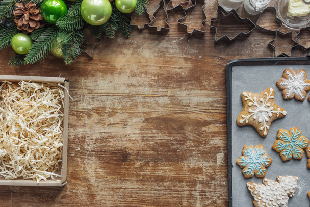 flat lay with christmas cookies on baking pan, christmas wreath, cardboard box and cookie cuttrers on wooden surface - Photo, Image