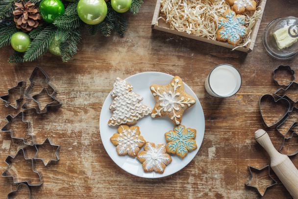 flat lay with baked cookies on plate on wooden surface with christmas decorative wreath and glass of milk - Photo, image