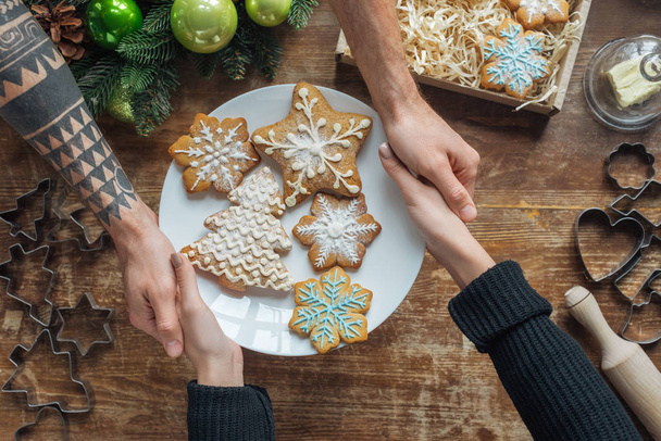 partial view of man and woman holding plate with homemade cookies on wooden tabletop with decorative christmas wreath - Photo, Image