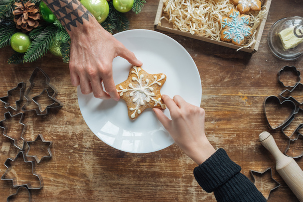 partial view of man and woman holding homemade cookie on wooden tabletop with decorative christmas wreath - Photo, Image