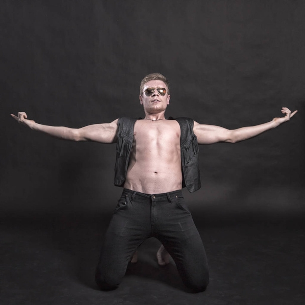 Handsome male bodybuilder in leather vest on a black background - Valokuva, kuva