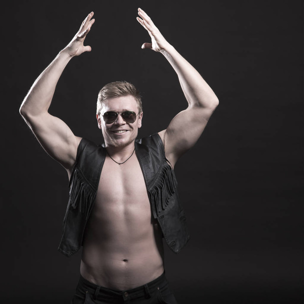 Handsome male bodybuilder in leather vest on a black background - Foto, afbeelding