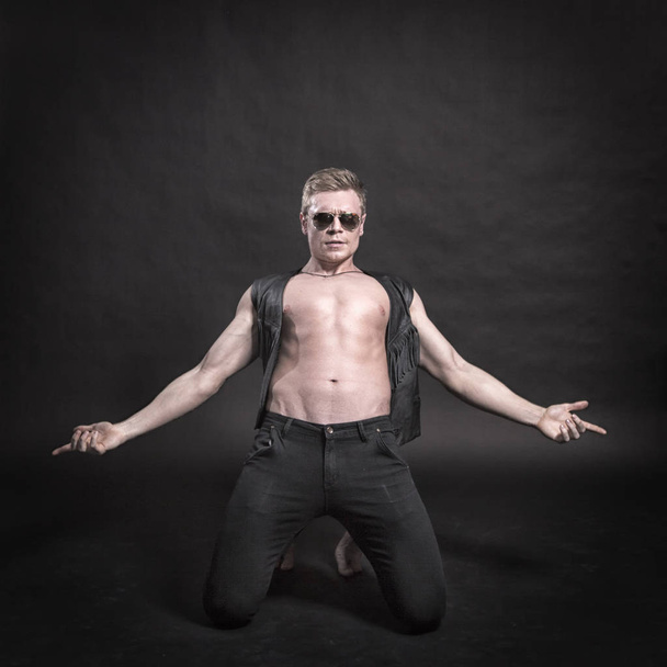 Handsome male bodybuilder in leather vest on a black background - Foto, Imagem