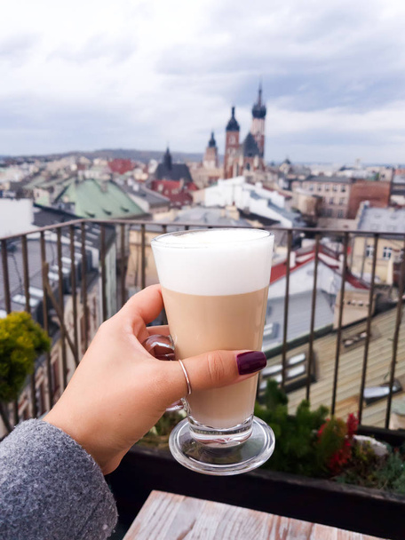 Woman holding coffee cup in cafe on a roof with view to St. Marys Church Krakow , Poland at the morning - Photo, Image