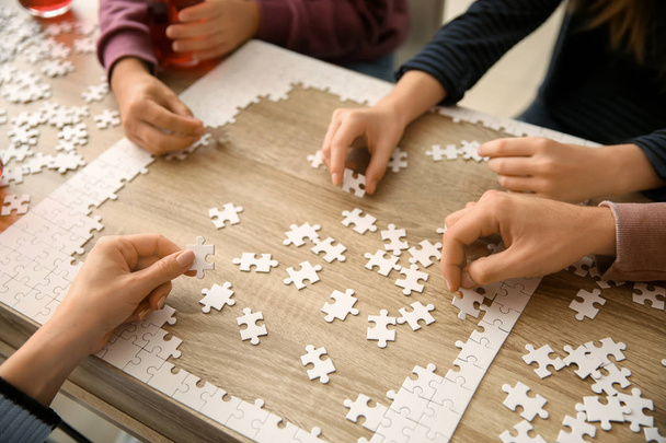 Группа людей собирает головоломку на деревянном столе
 - Фото, изображение