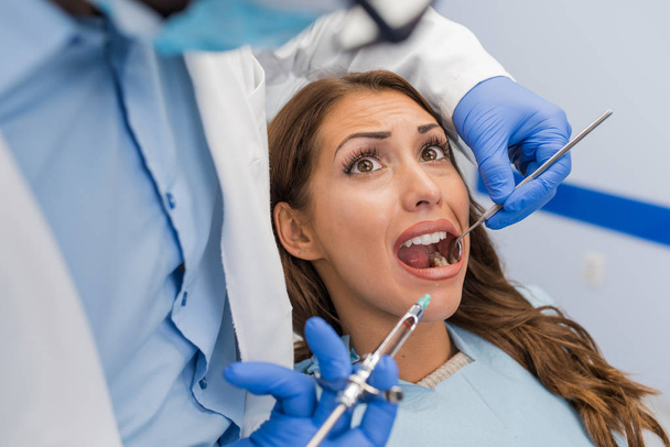Woman looking scared as dentist puts syringe in his mouth - Photo, Image
