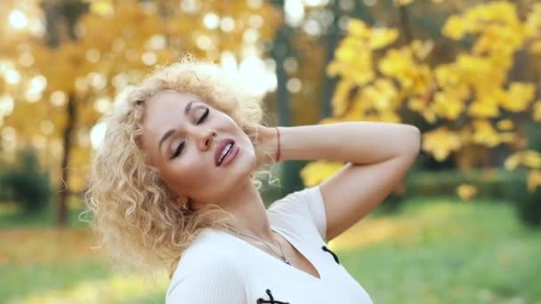 Krásná blondýnka dotýká kudrnaté vlasy, procházky v podzimním parku. - Záběry, video
