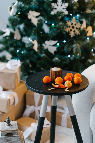 μανταρίνια σε μικρό τραπέζι στην αίθουσα με το χριστουγεννιάτικο δέντρο  - Φωτογραφία, εικόνα