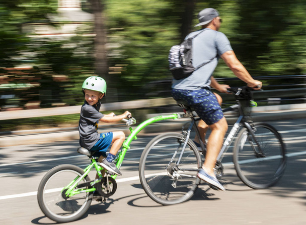 Nueva York, Estados Unidos - 15 de agosto de 2018: Padre e hijo viajando en bicicleta con un accesorio en la espalda en el parque central con un fondo borroso
. - Foto, Imagen