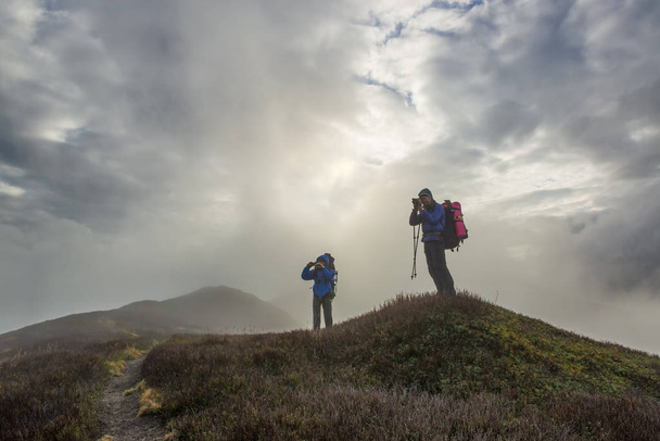 Gli escursionisti scattano foto sulla cima di una montagna con nuvole intorno e sotto. Escursioni in autunno
 - Foto, immagini