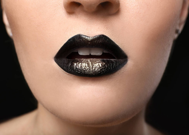 Jonge vrouw met extravagante make-up in zwarte en gouden tinten, close-up - Foto, afbeelding