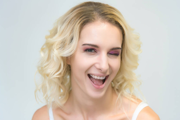 Beauty portrait of a beautiful blonde girl on a white background with perfect makeup. Beauty style model is right in front of the camera and looks happy. - Фото, изображение