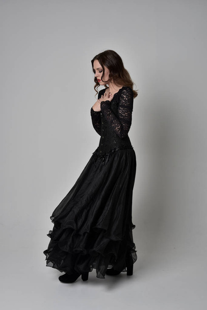 full length portrait of brunette girl wearing long black lace gown wit corset. standing pose, isolated on grey studio background. - Fotoğraf, Görsel