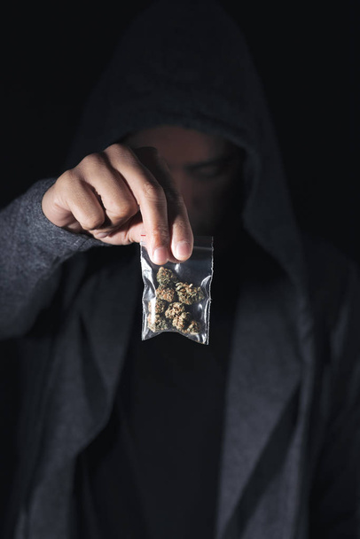 Крупный план молодого кавказца с пластиковым пакетом с марихуаной в руке
 - Фото, изображение