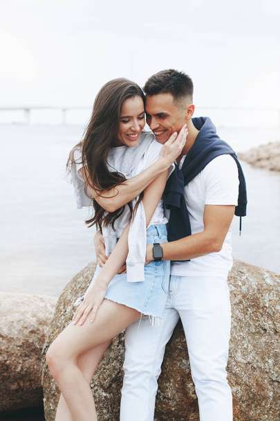 Young beautiful positive couple sitting on stone by sea. Lifestyle concept - Photo, Image