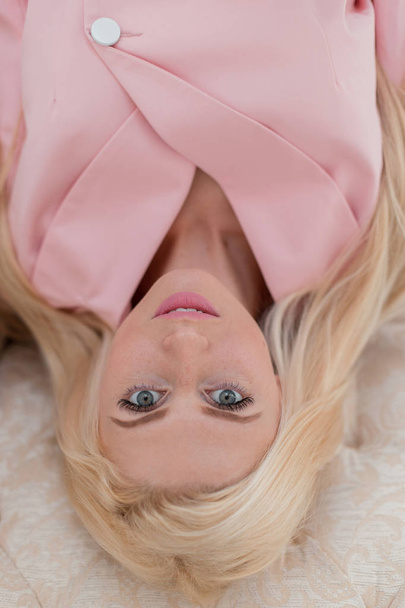 Bella giovane donna con lentiggini in un abito alla moda rosa si trova su un divano vista dall'alto
 - Foto, immagini
