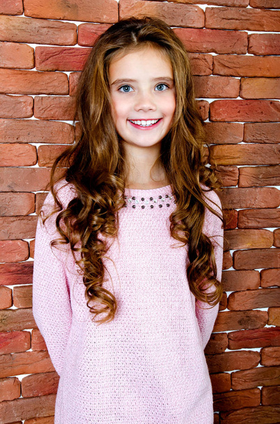Portrait of adorable smiling standing little girl child near the brick wall - Fotó, kép