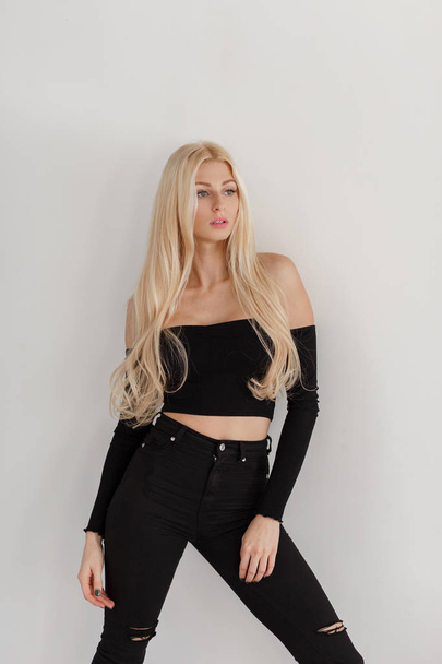 Young beautiful blond woman with freckles in black fashionable clothes stands near the white wall - Foto, Bild